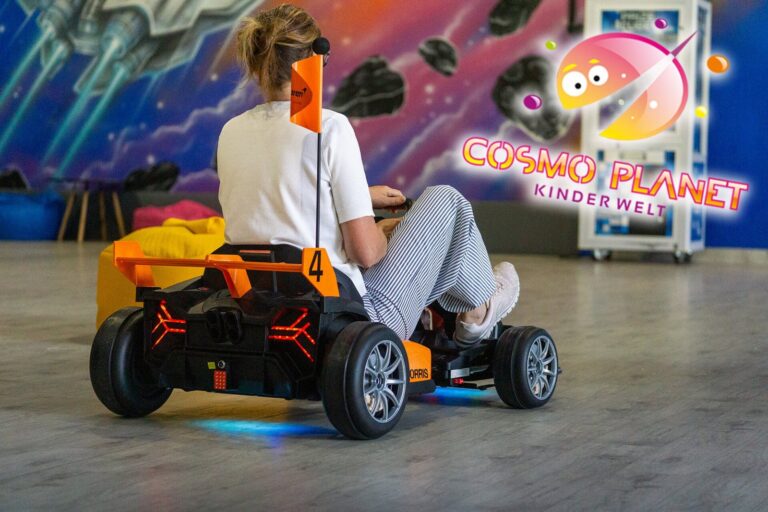 Besucherin fährt mit einem Elektro-Kart vor der Weltraum-Wand im Cosmo Planet Forst
