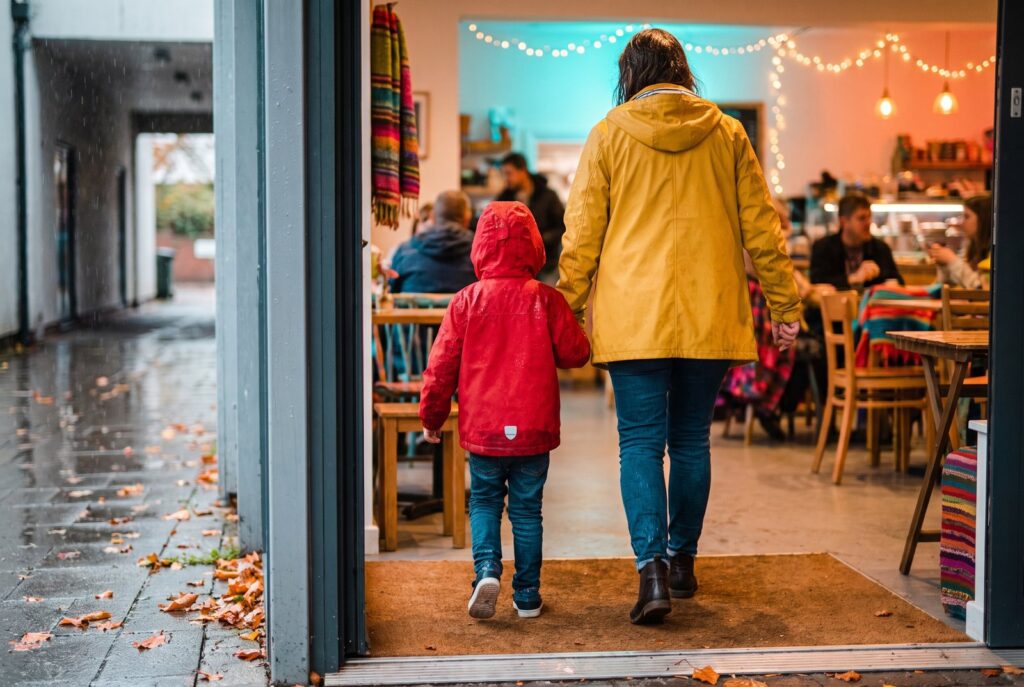 Mutter und Kind in Regenjacken kommen an einem Herbsttag ins Warme